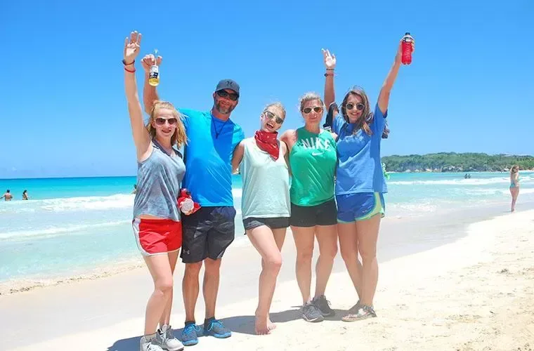Group of guests with their arms up on a white sand beach