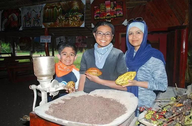 Guests holding cacao pods beside a grinder during the farm stop