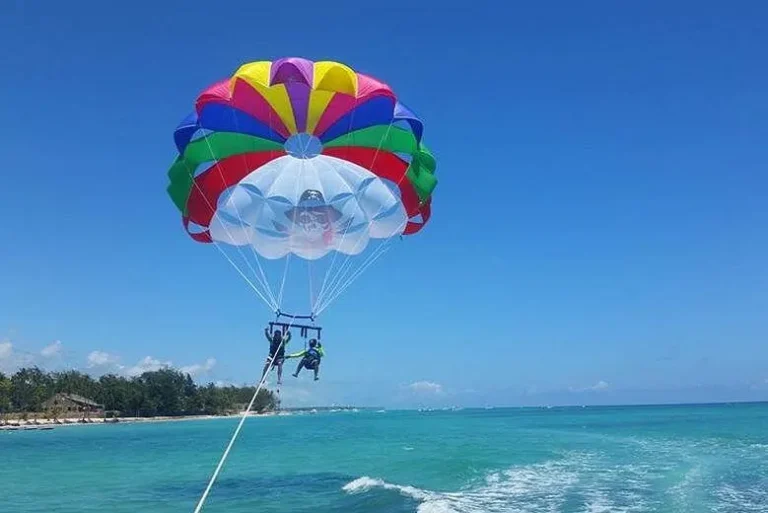 Two riders under a rainbow parasail above the Caribbean